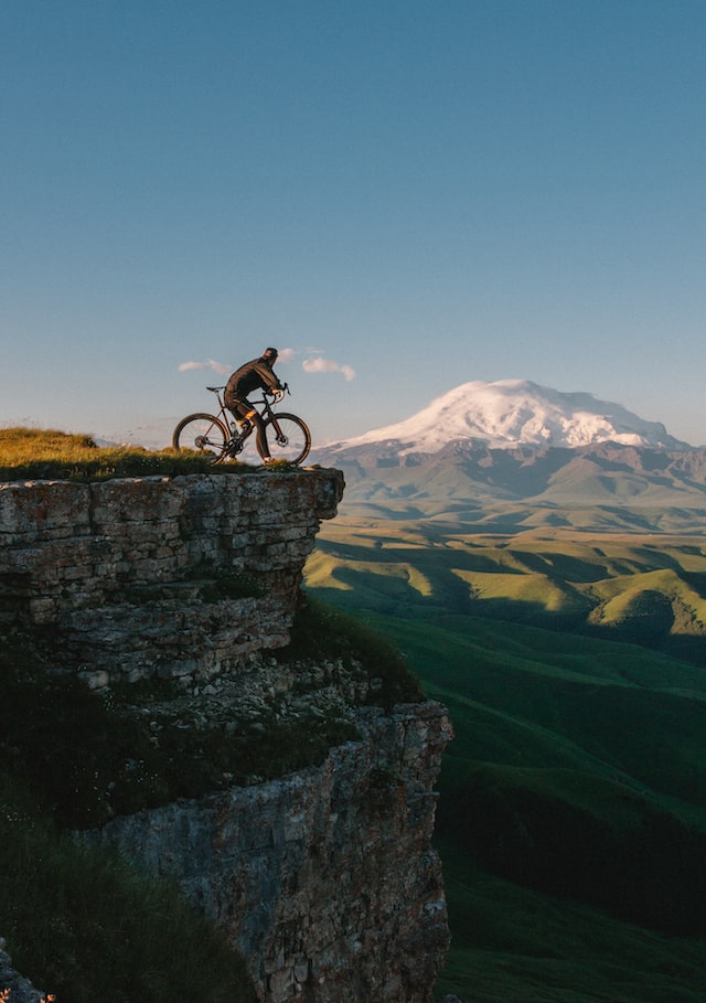 Fahrradfahrer steht mit seinem Fahrrad an einer Klippe und genießt die Aussicht auf die Berglandschaft.