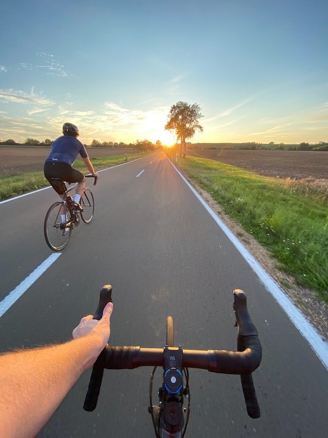 Zwei Rennradfahrer fahren bei Sonnenuntergang Straße entlang. 