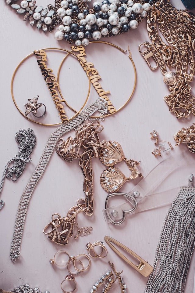 Verschiedene Schmuckstücke wie Kreolen, Ohrringe, Ketten in silber, gold und rosegold liegen auf einer rosa Fläche