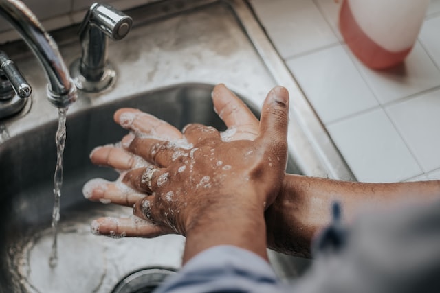 Person wäscht sich die Hände unter fließendem Wasser in einem Waschbecken. 