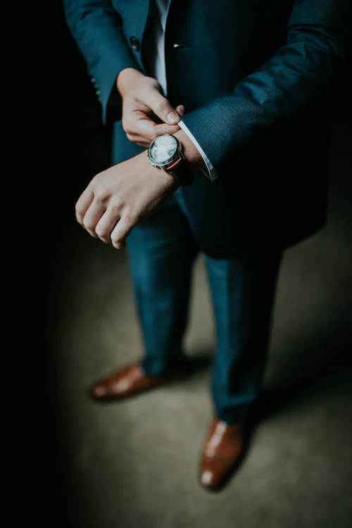 Mann im Anzug richtet sich den Ärmel. Er trägt eine Uhr und braune Schuhe.