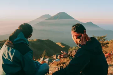 Zwei sitzende Personen in Wanderkleidung. Im Hintergrund ist ein Berg zu sehen.
