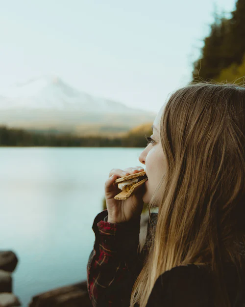 Mädchen isst Brot und Blickt in die Berg- und Seenlandschaft. 