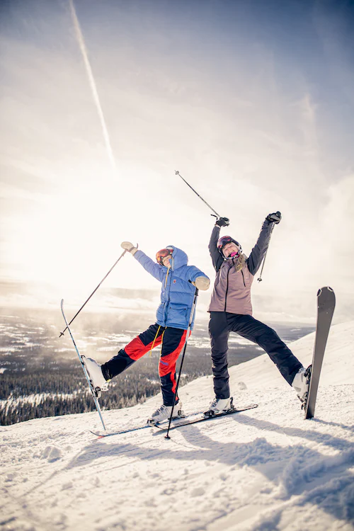 Zwei Personen in Skiausrüstung posieren in Richtung Kamera. 