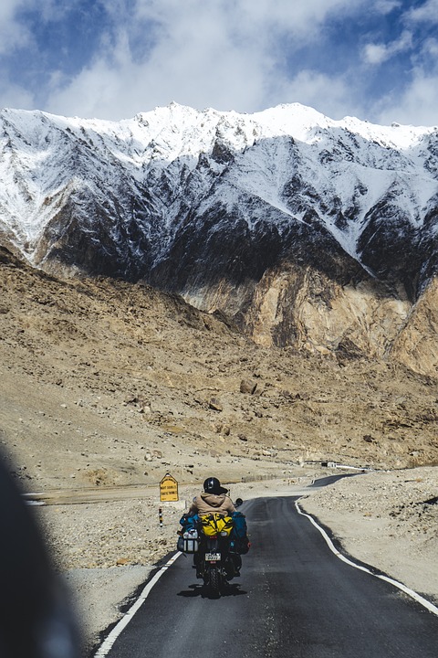 Motorrad fährt auf einer Straße. Im Hintergrund sind beschneite Berge zu sehen. 