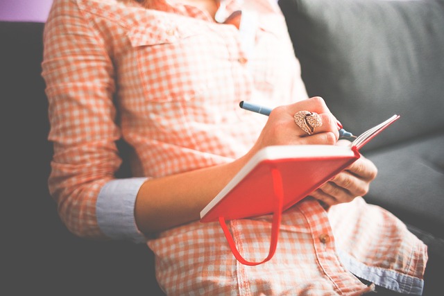 sitzende Frau in karierter Bluse schreibt in einen roten Notizblock