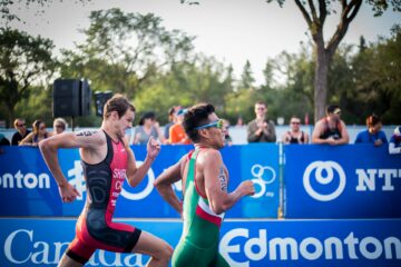 Zwei Triathlon-Läufer laufen um die Wette. Im Hintergrund sind Zuschauer zu sehen